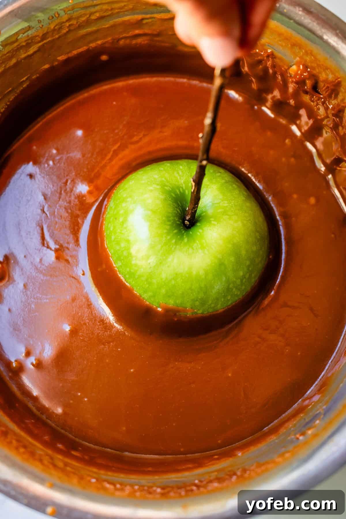 My Ultimate Caramel Apple 3 A crisp green apple, impaled on a sturdy stick, being carefully dipped into a pot of glistening, amber caramel sauce.