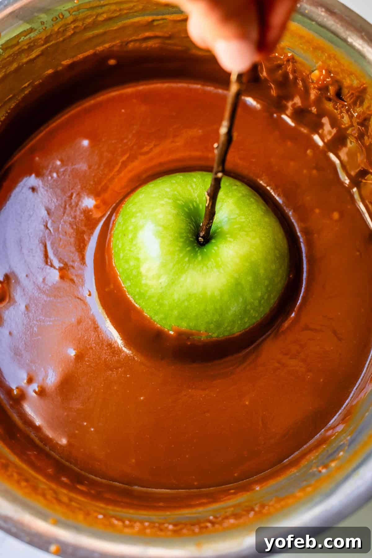 My Ultimate Caramel Apple 23 A crisp Granny Smith apple, impaled on a stick, gracefully submerged halfway into a pot filled with rich, golden caramel sauce.