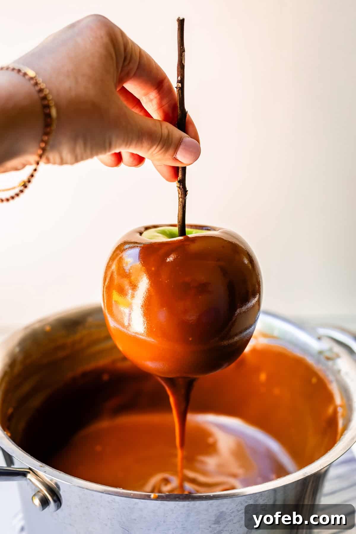 My Ultimate Caramel Apple 26 A hand holding a caramel-coated apple above the pot, allowing excess caramel to gracefully drip back down, ensuring an even layer.