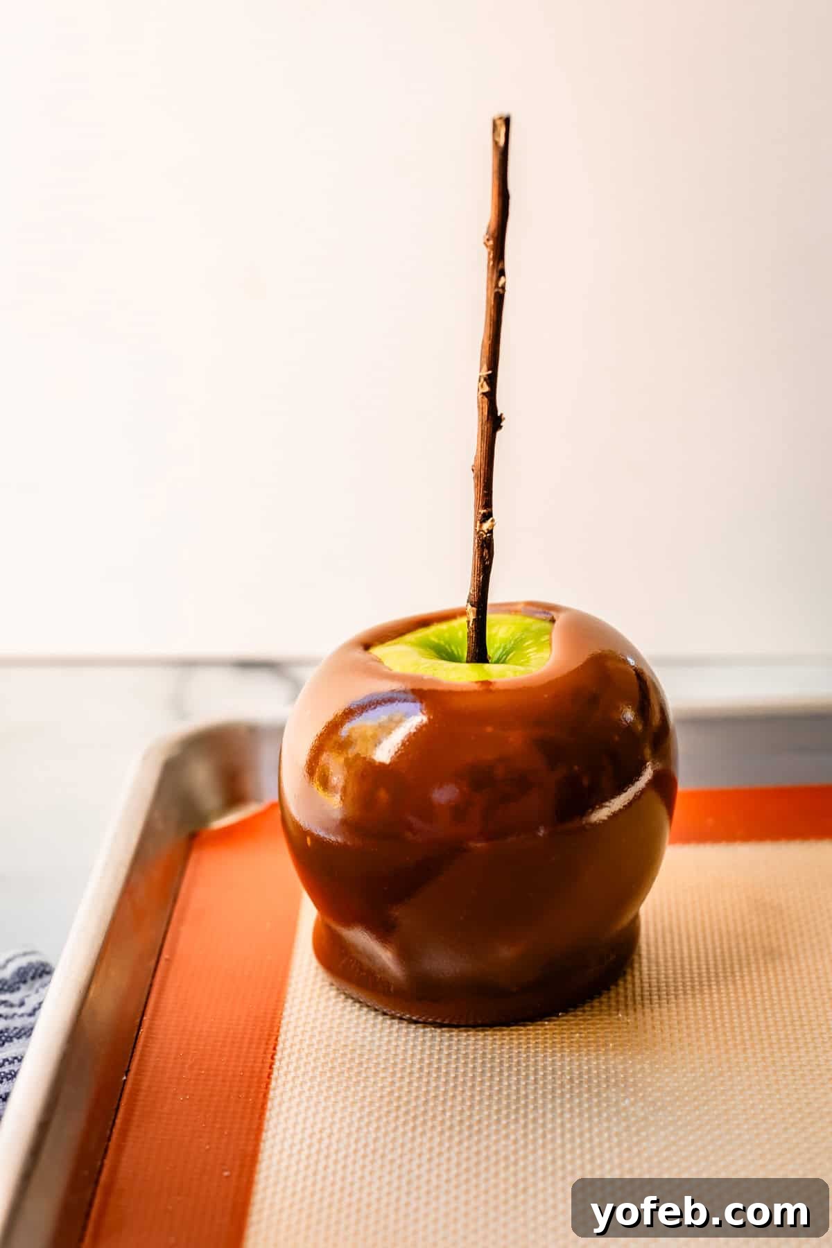My Ultimate Caramel Apple 28 A freshly dipped caramel apple, complete with a stick, resting on a silpat baking mat to cool and set, demonstrating perfect adherence.