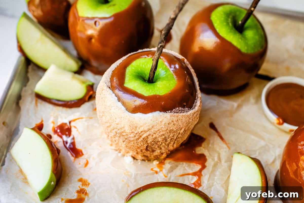 My Ultimate Caramel Apple 31 A close-up of a finished caramel apple, dipped in white chocolate and coated in cinnamon sugar, prominently displayed with plain caramel apples in the background, all resting on a silpat mat.