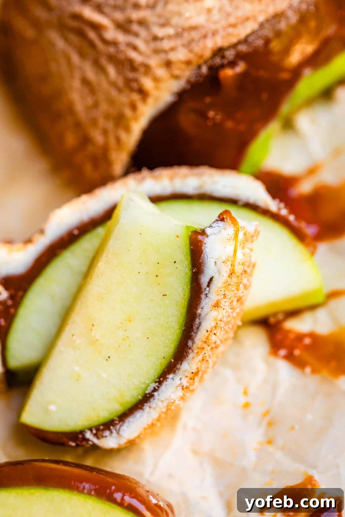 My Ultimate Caramel Apple 34 Stacked snickerdoodle-coated apple slices with a bite taken out of the top slice, showcasing the creamy caramel and crisp apple inside.