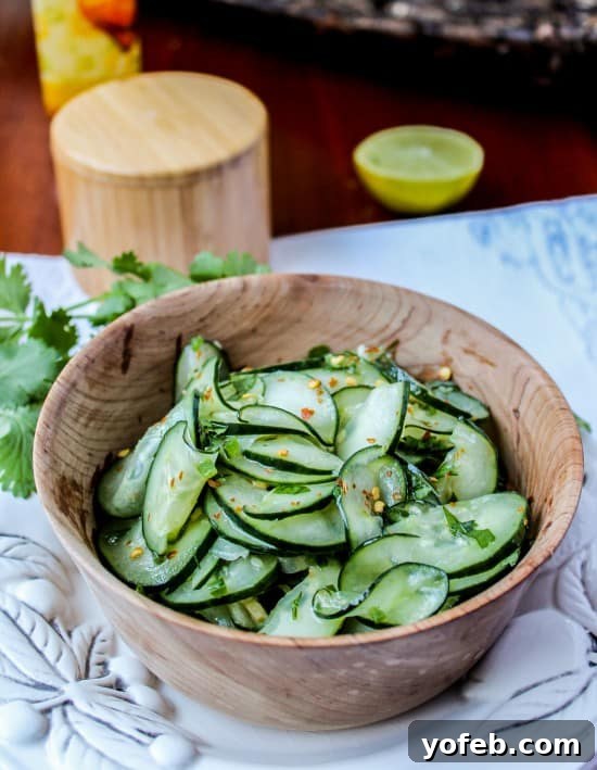 Fresh Cilantro Lime Cucumber Salad with Garnish Overhead shot of Mexican cucumber salad in a wooden bowl, surrounded by fresh cilantro, lime, and a white serving platter.