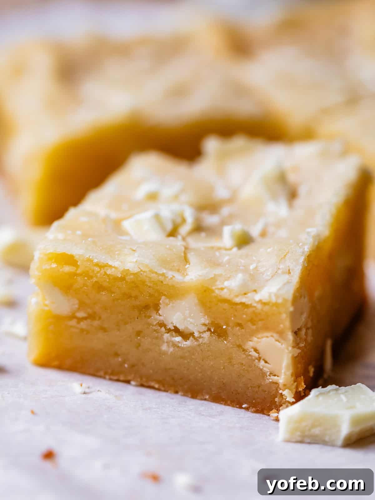 Irresistible White Chocolate Brownies 20 A rectangular piece of white chocolate brownie, showcasing the visible white chocolate chunks within and on top, emphasizing its rich texture.