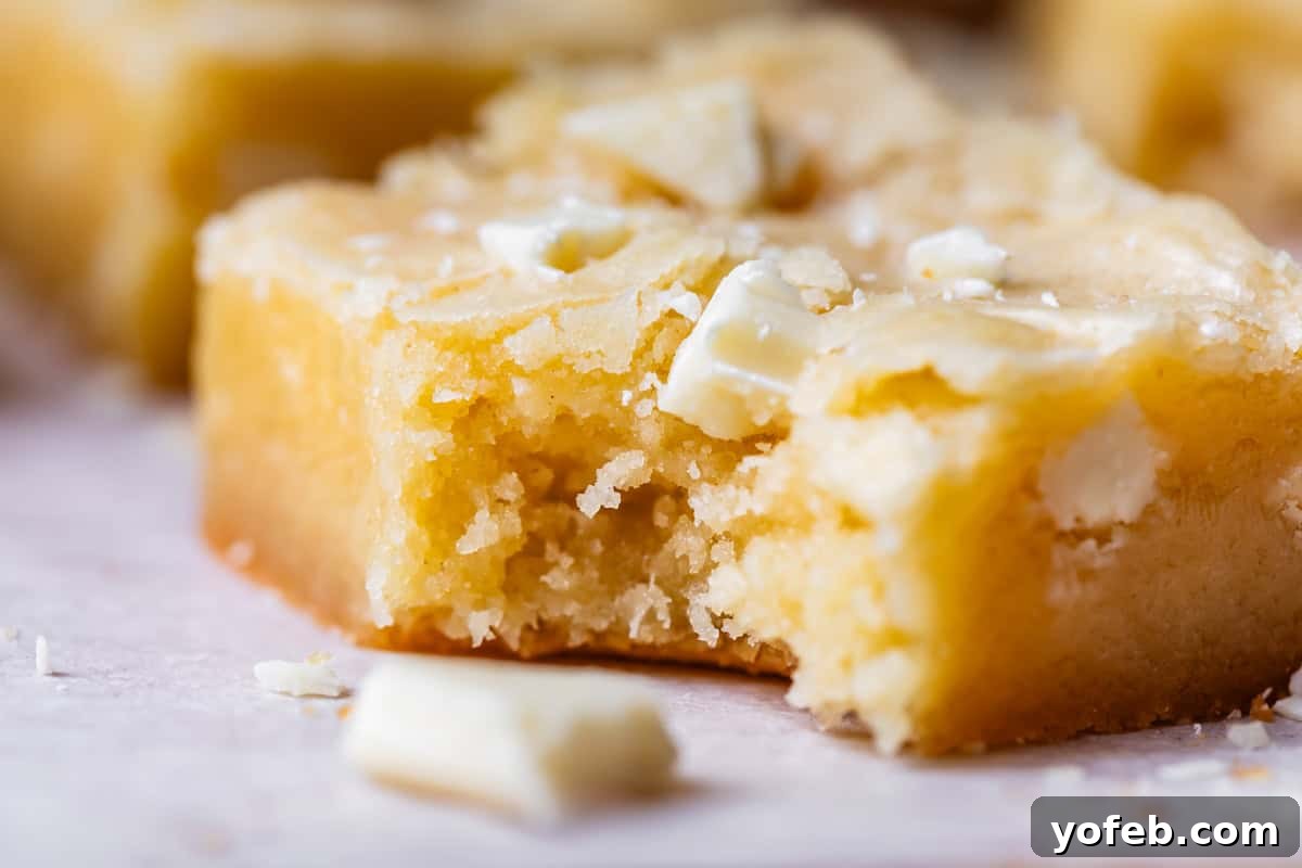 Irresistible White Chocolate Brownies 21 Close-up side view of a white chocolate brownie with a bite missing, showing its luscious texture and creamy white chocolate chunks, ready for enjoyment.