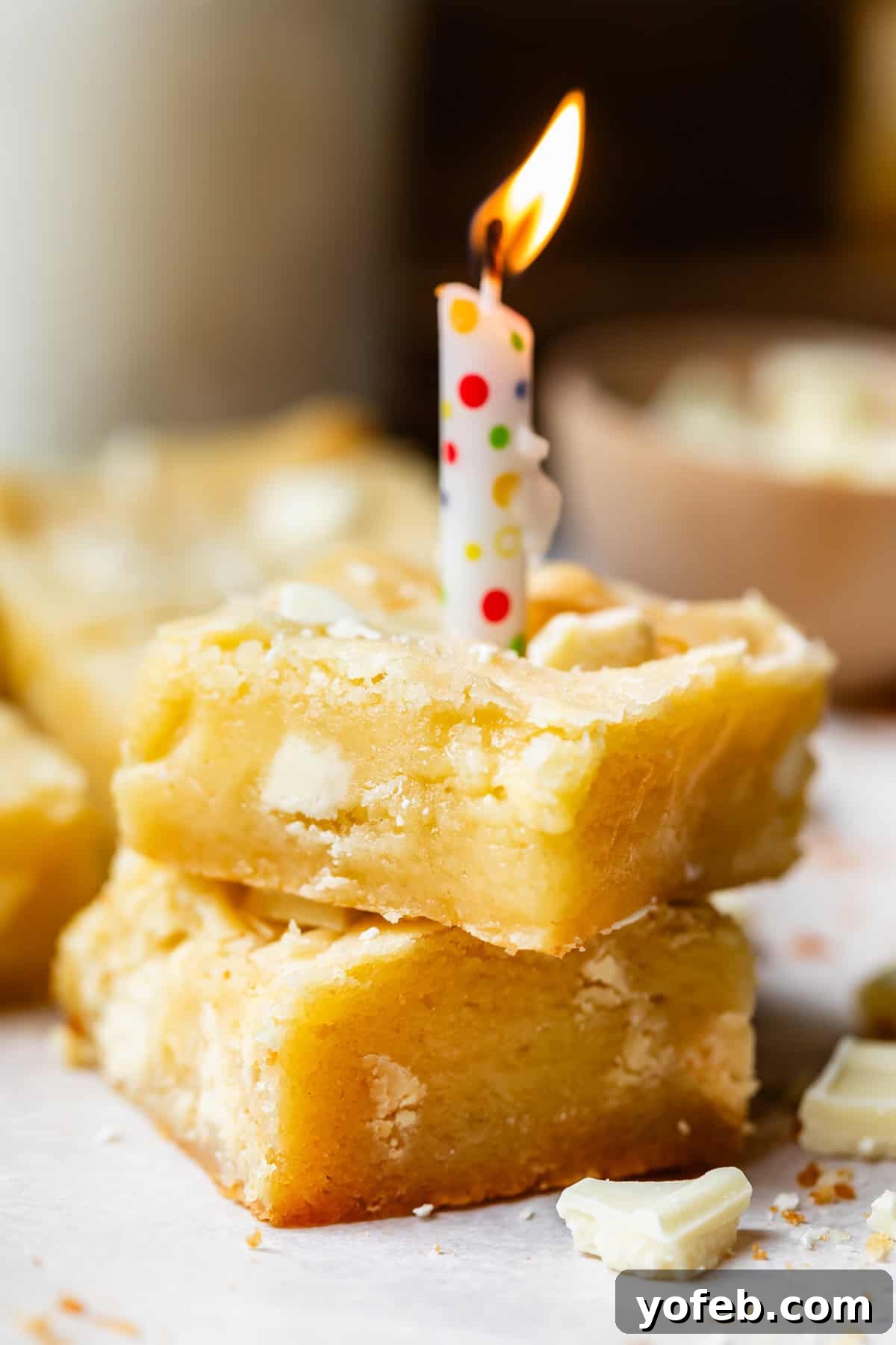 Irresistible White Chocolate Brownies 5 Two white chocolate brownies stacked, with a lit birthday candle in the top one, symbolizing a celebratory moment for the blog's anniversary.