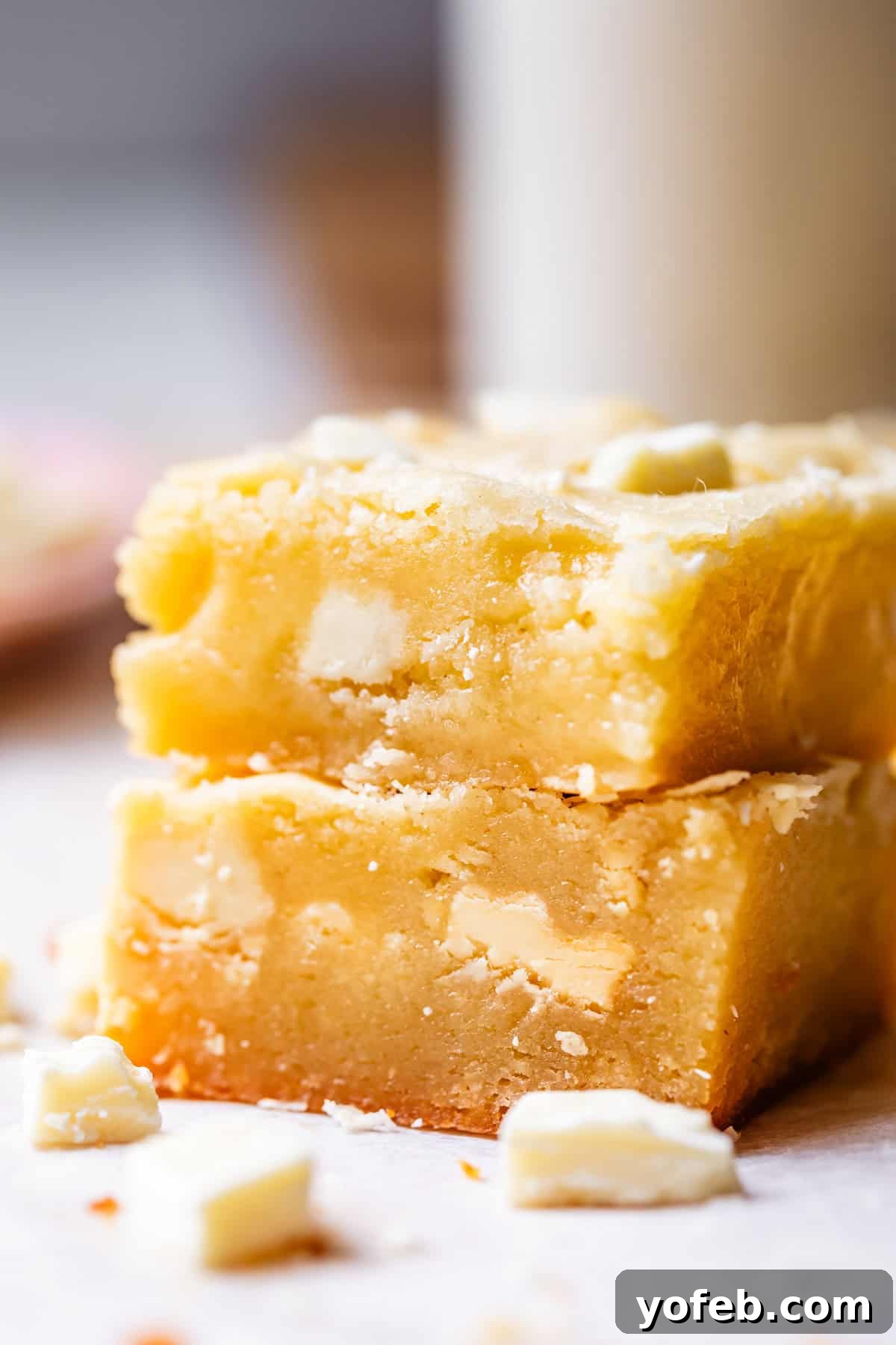 Irresistible White Chocolate Brownies 7 Side view of two stacked square pieces of fudgy white chocolate brownies, revealing their luscious layers and texture.