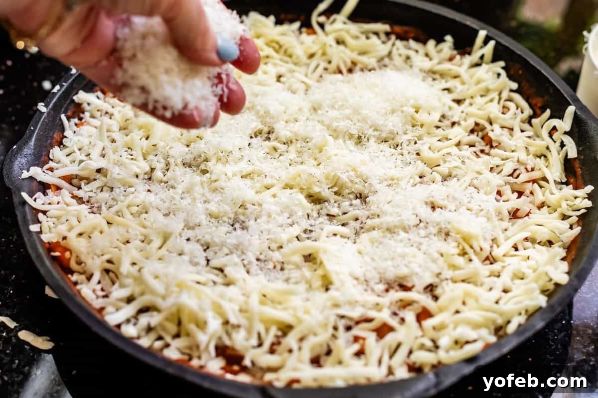 Rustic Tomato, White Bean & Cheese Bake 13 A hand sprinkles finely shredded Parmesan cheese over the top of the mozzarella layer, preparing the bake for its final broiler finish.