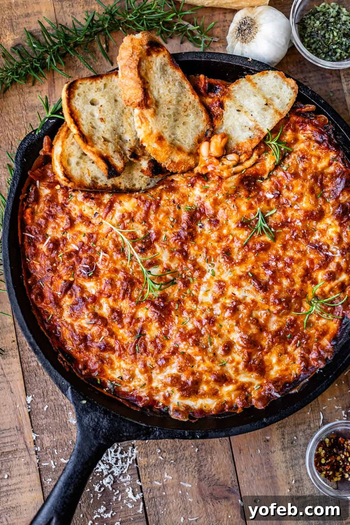 Rustic Tomato, White Bean & Cheese Bake 14 A glorious cast iron skillet on a wooden table, filled with the golden-brown, cheesy white bean tomato bake, with several slices of sourdough bread nestled invitingly within.