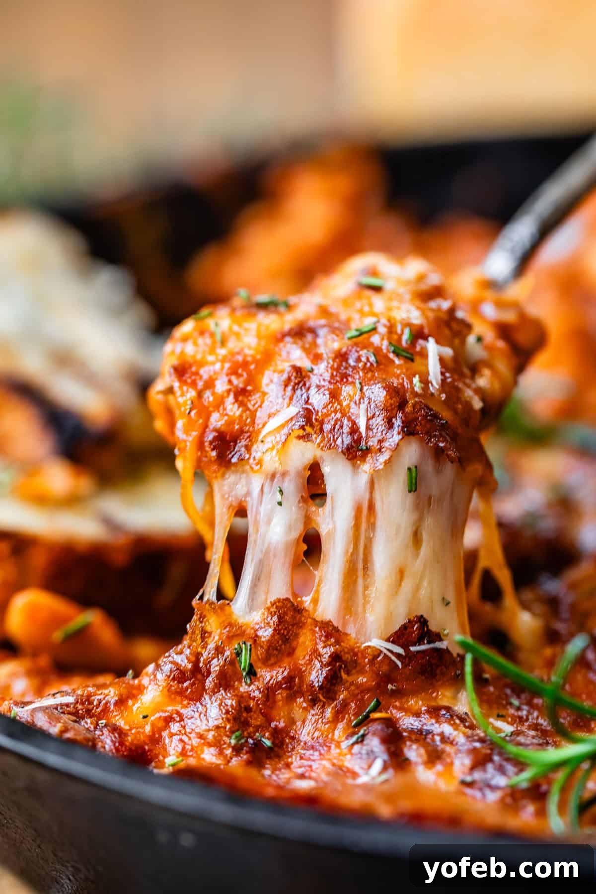 Rustic Tomato, White Bean & Cheese Bake 6 A spoon lifts a portion of the Cheesy White Bean Tomato Bake, creating a long, appetizing stretch of melted cheese.