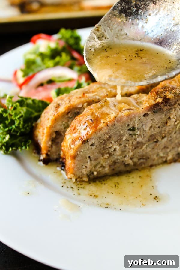 1770 House Meatloaf with Garlic Sauce by Ina Garten. Tender, moist, and flavorful with a delectable garlic sauce. #meatloaf #inagarten #garlic #comfortfood #barefootcontessa #groundbeef #sauces Slices of perfectly cooked meatloaf, glistening with rich garlic sauce, alongside a fresh side salad on a white plate, ready to be enjoyed.