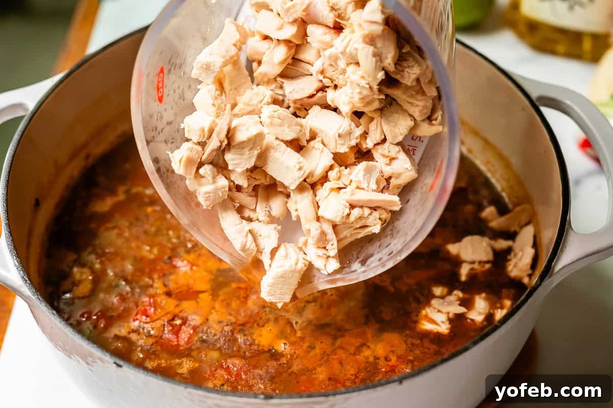 No-Fuss Chicken Tortilla Soup 19 a large measuring cup of chopped chicken being poured into the pot of soup.