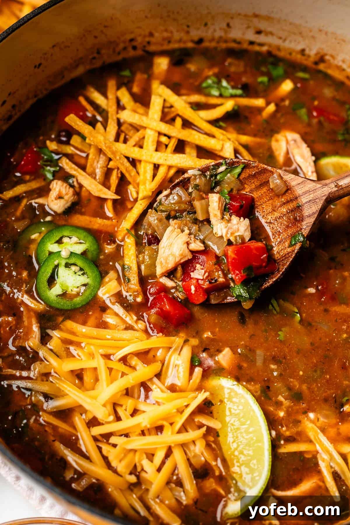 No-Fuss Chicken Tortilla Soup 24 wooden spoon lifting some soup out of a bowl that is garnished with cheese and tortilla.