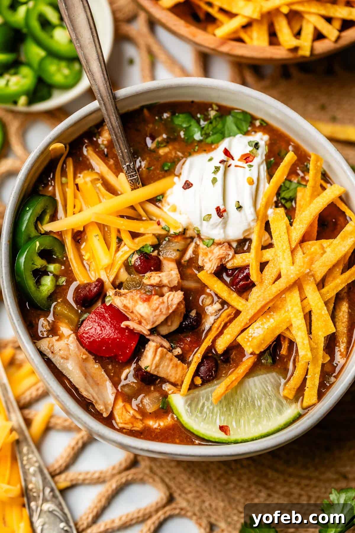 No-Fuss Chicken Tortilla Soup 25 ceramic bowl filled to the brim with soup and toppings like tortilla strips and cheese.