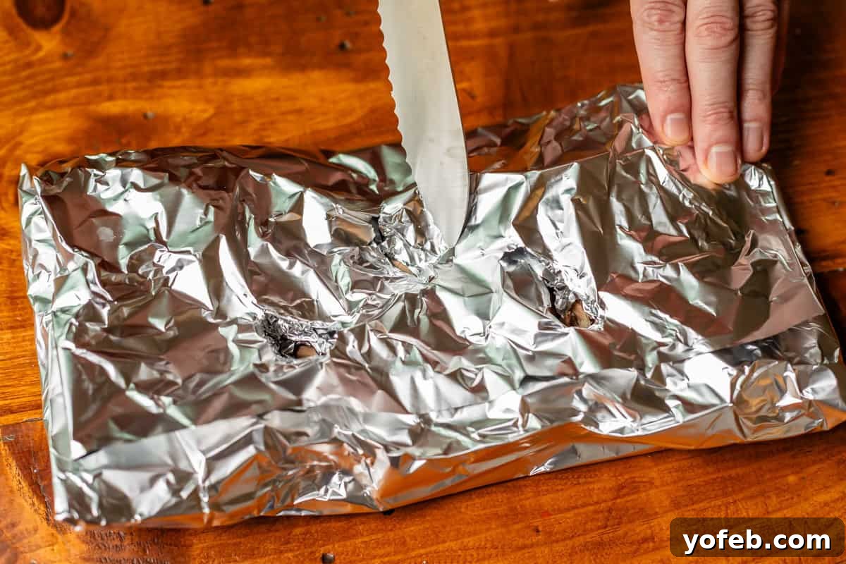 Texas Brisket: Oven-Perfected Tenderness 21 hand holding down a foil pouch filled with wood chips while knife cuts a slit in it.