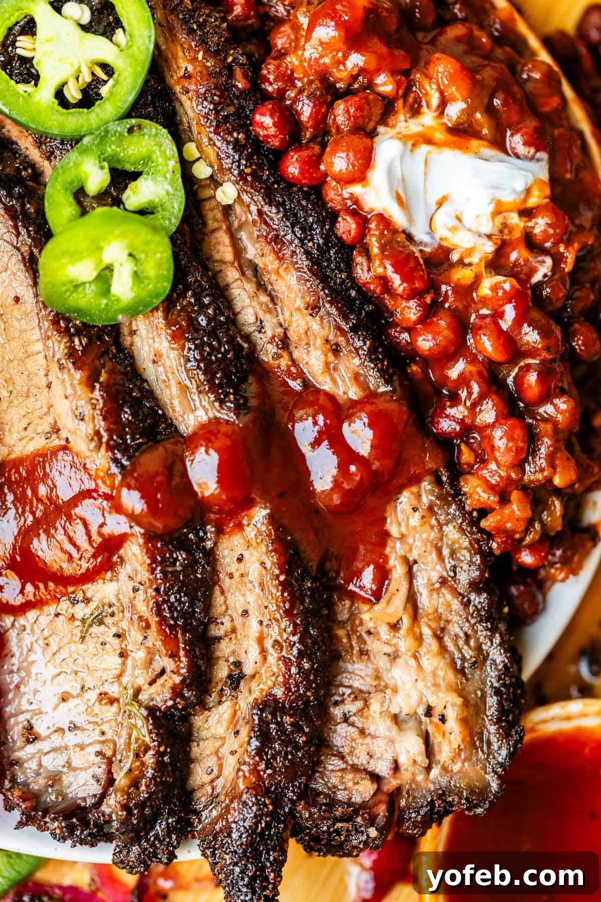 Texas Brisket: Oven-Perfected Tenderness 34 Overhead shot of beef brisket with barbecue sauce, beans, and jalapeño on a white plate.