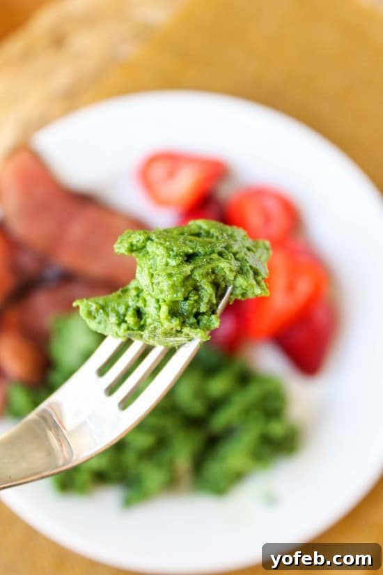 Garden Green Eggs and Ham 5 A forkful of vibrant green scrambled eggs, poised against a background of a full plate featuring green eggs, Black Forest ham, and fresh strawberries.