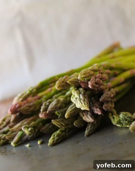 Crisp Asparagus and Tomato Medley 8 Fresh green asparagus spears lined up neatly on a rustic wooden cutting board, ready for prep work.