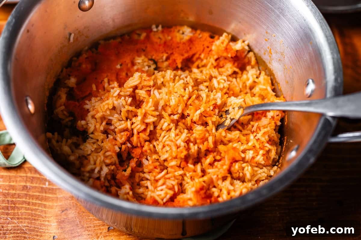 The Ultimate Homemade Mexican Rice 11 fork fluffing the sauce back into the rice in a metal pot.