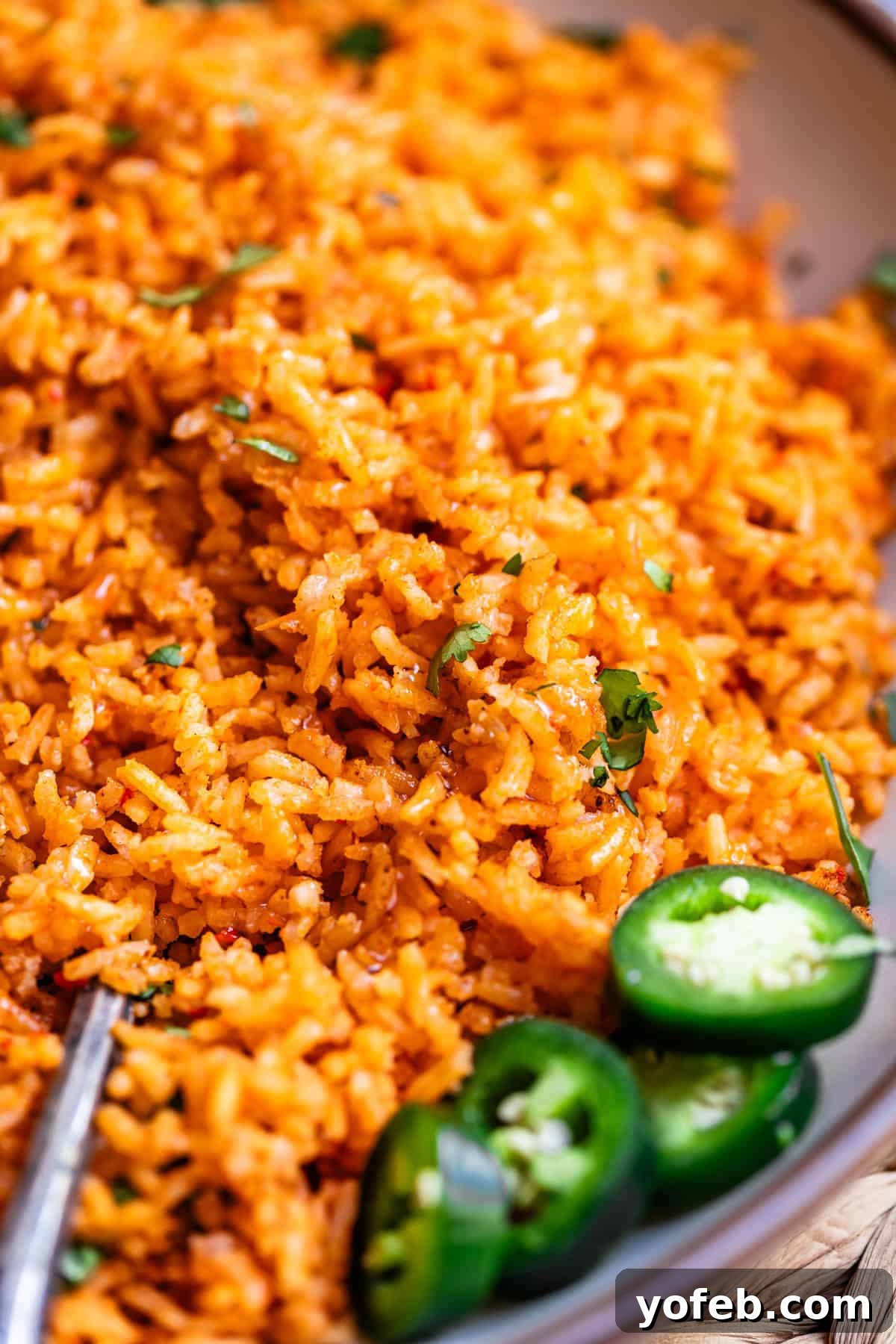 The Ultimate Homemade Mexican Rice 16 a spoon in a large serving of Mexican rice with jalapeno garnish.