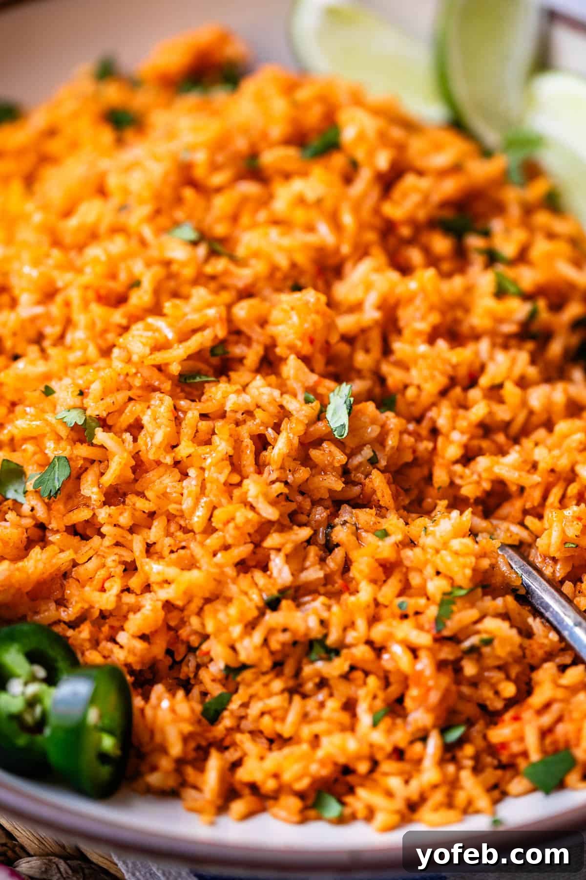The Ultimate Homemade Mexican Rice 5 a spoon in a serving platter filled with Mexican rice and jalapeno and cilantro garnish.