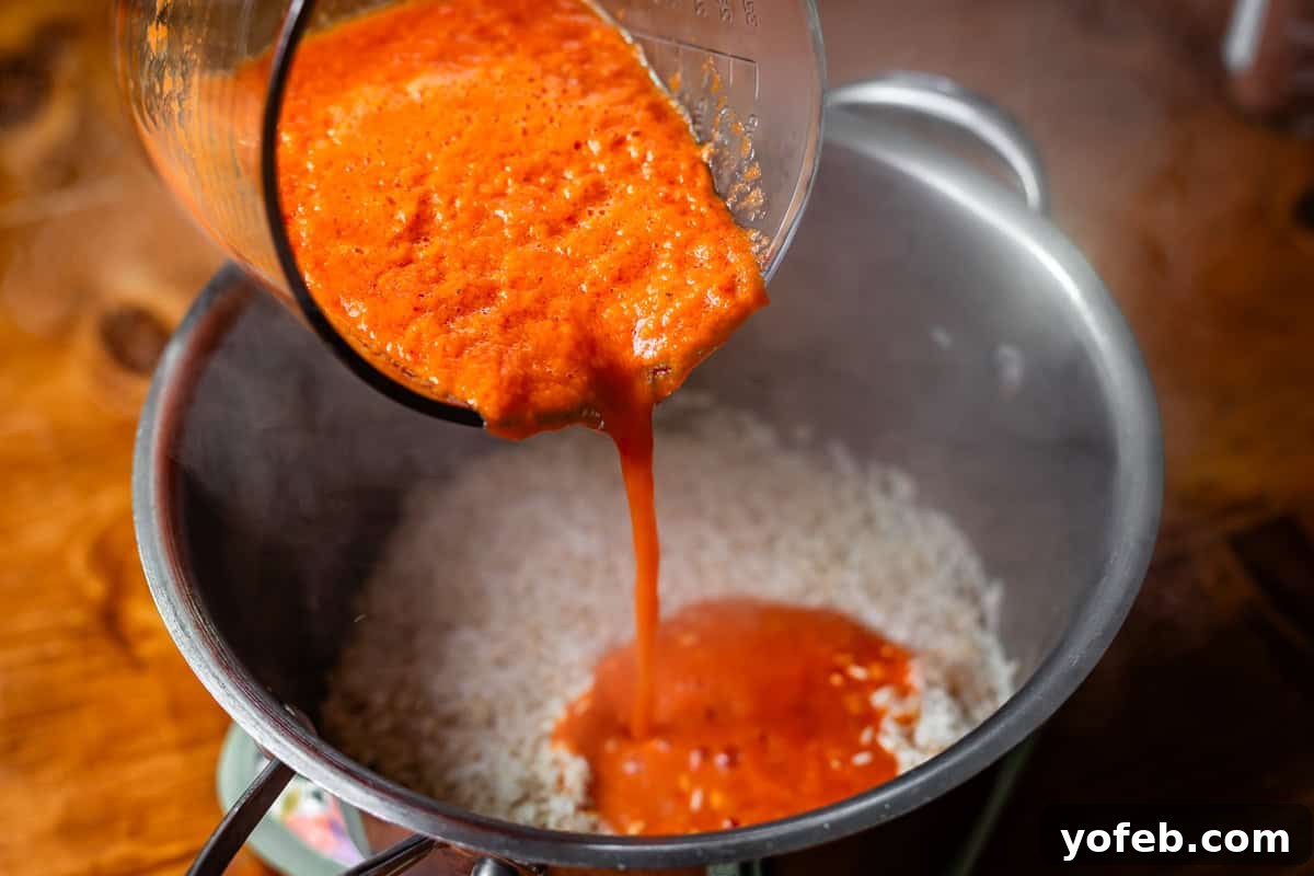 The Ultimate Homemade Mexican Rice 9 tomato sauce being poured from blender into metal pan with rice in it.
