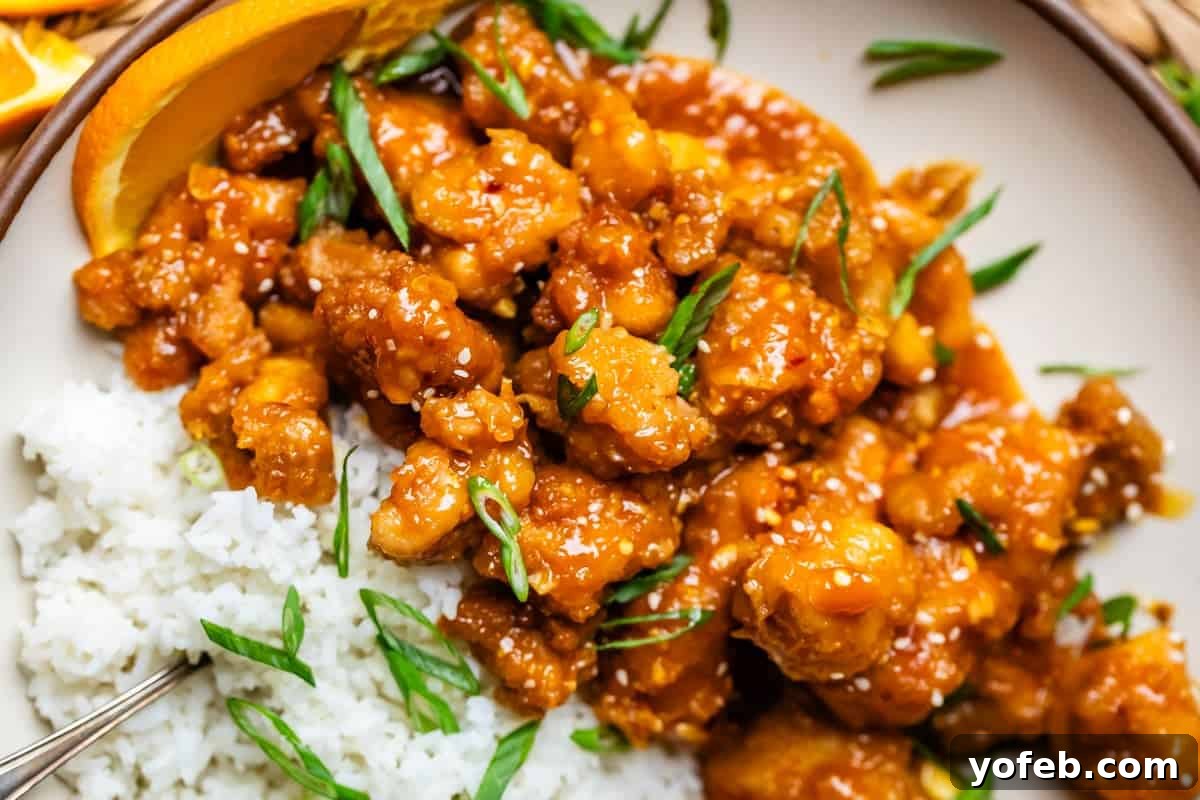 Ultimate Orange Chicken 18 A dinner plate featuring fluffy white rice alongside golden, crispy orange chicken, elegantly garnished with fresh green onions.
