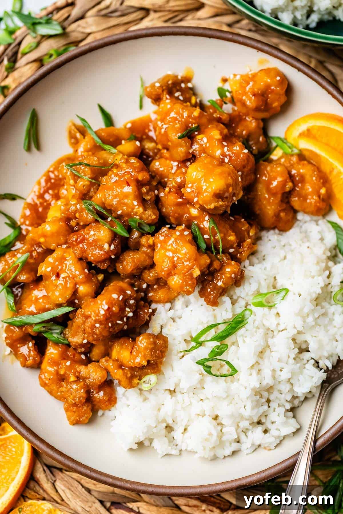 Ultimate Orange Chicken 19 A dinner plate featuring fluffy white rice alongside golden, crispy orange chicken, elegantly garnished with fresh green onions.