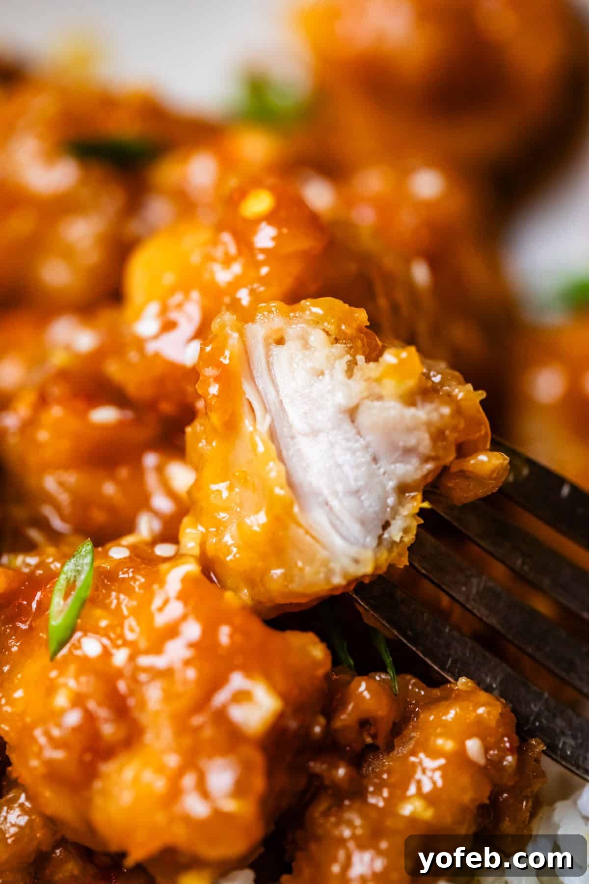 Ultimate Orange Chicken 20 Close up of a fork holding a piece of orange chicken, showing the tender, juicy interior of the chicken.