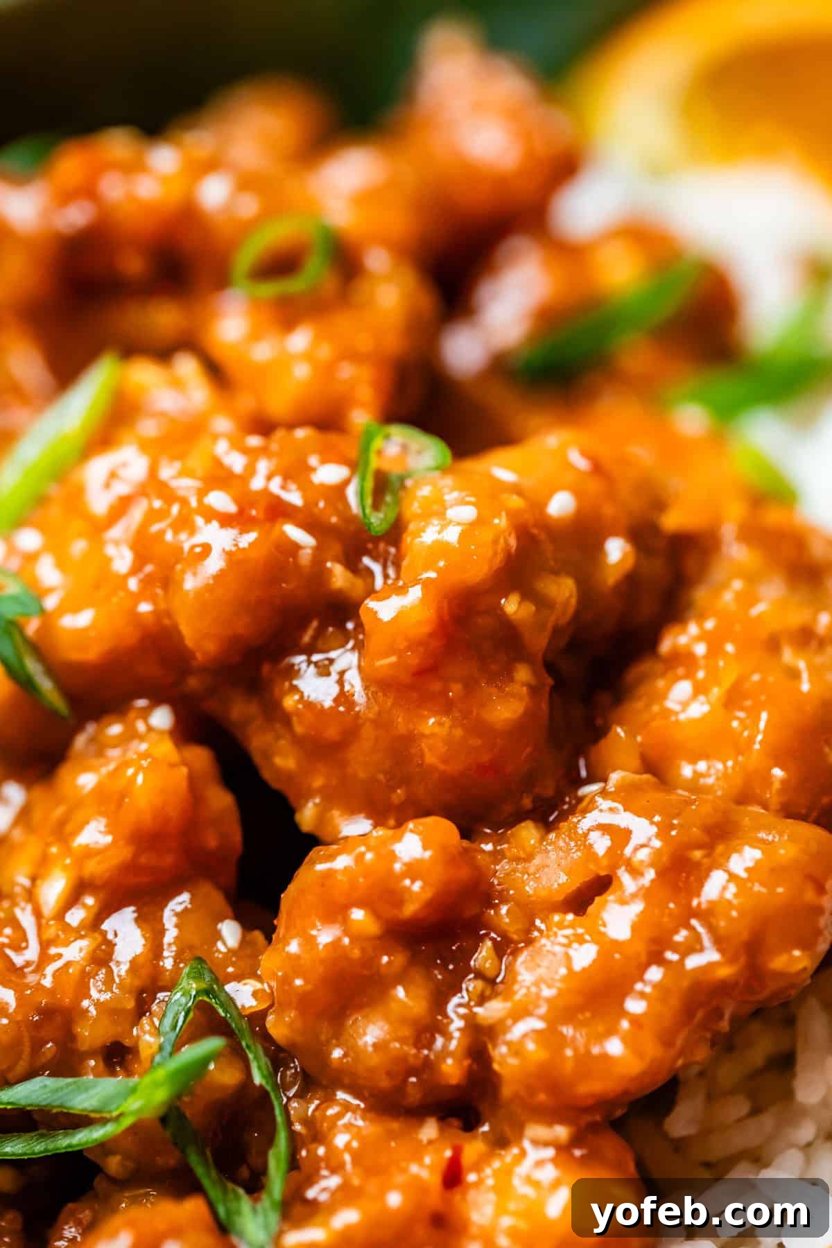 Ultimate Orange Chicken 3 Close up of a ceramic bowl filled with golden, crispy orange chicken, garnished with vibrant green onions.