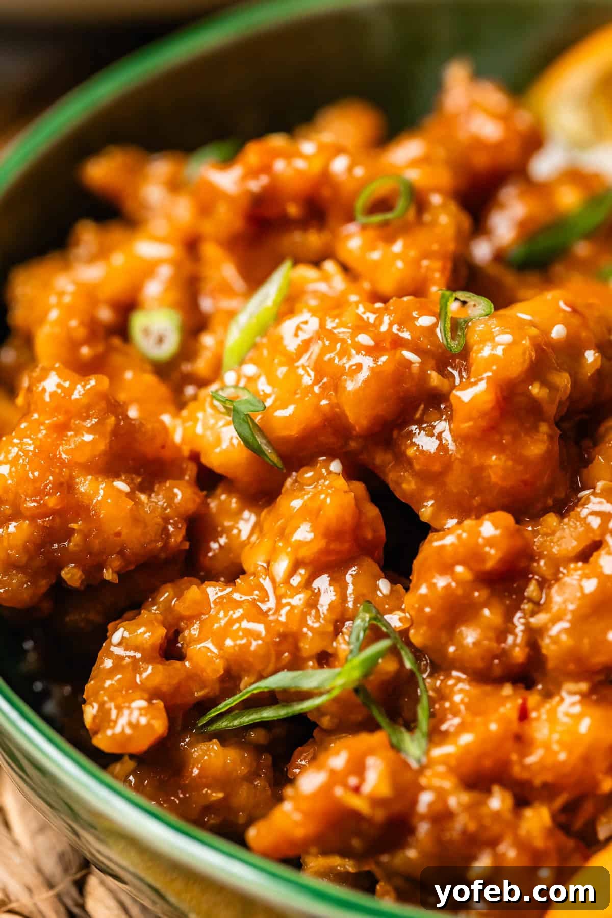 Ultimate Orange Chicken 4 Close up of a ceramic bowl filled with golden, crispy orange chicken, garnished with vibrant green onions, ready to be served.