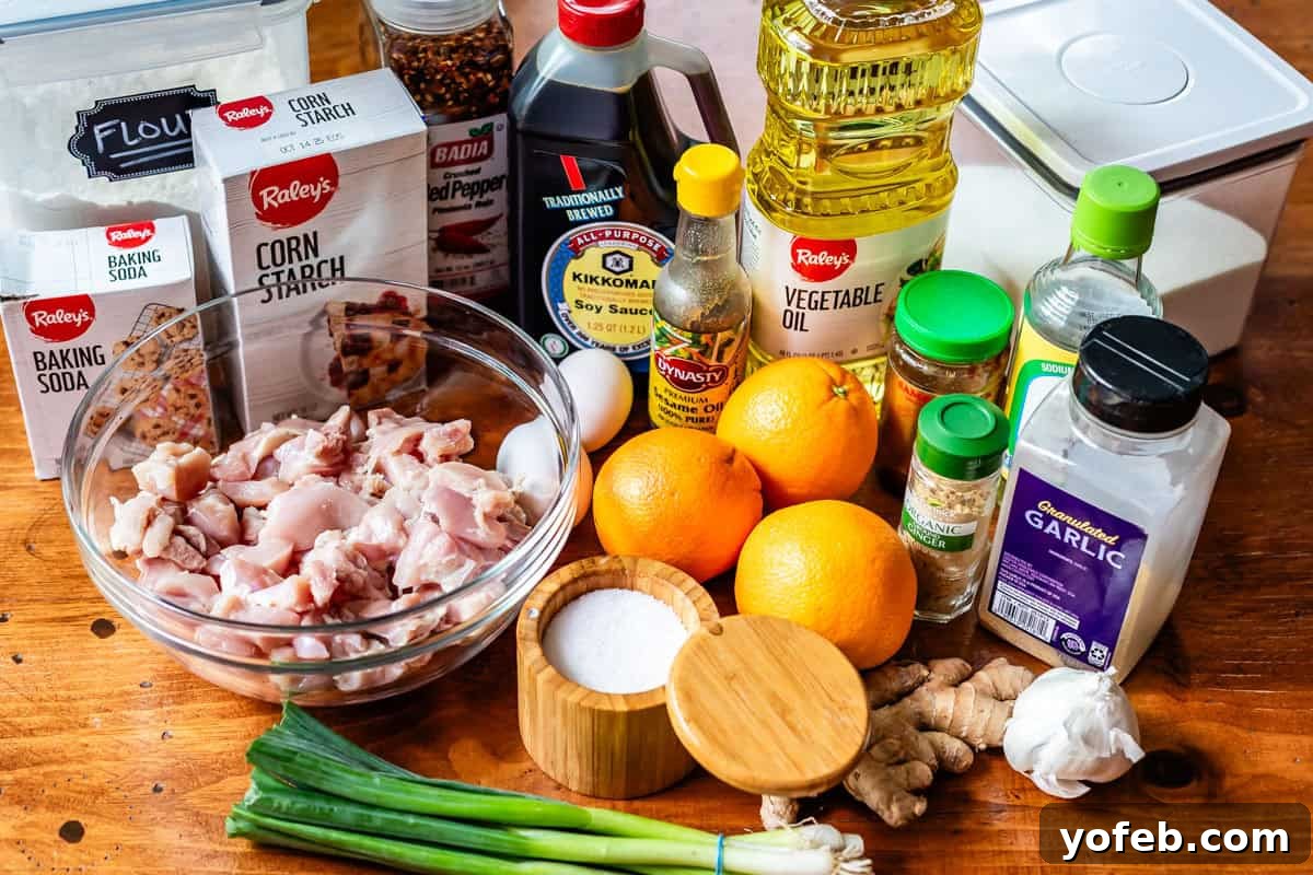 Ultimate Orange Chicken 6 A flat lay of fresh ingredients for Asian orange chicken, including chicken thighs, cornstarch, oranges, soy sauce, garlic, ginger, and green onions.