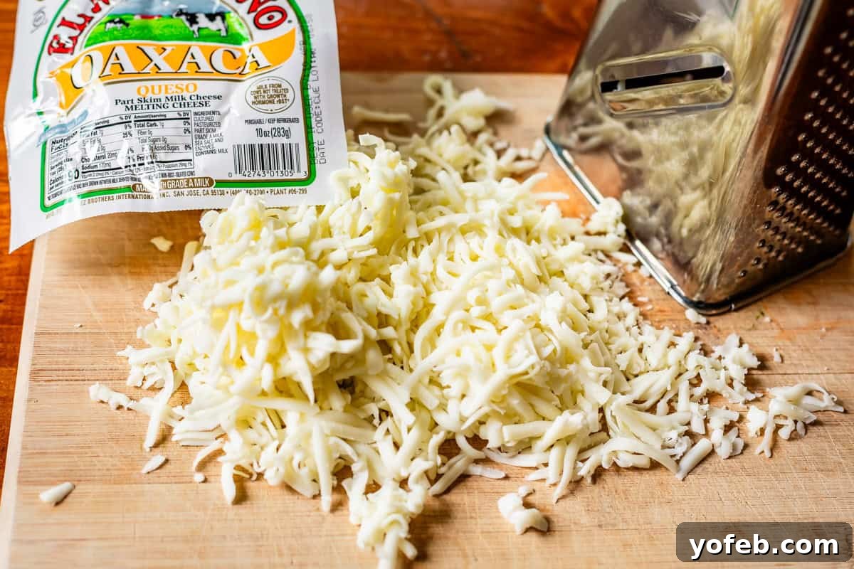 Yeni Gözdem Tavuk Enchilada 16 shredded Oaxaca cheese on a wood cutting board next to a box cheese grater.