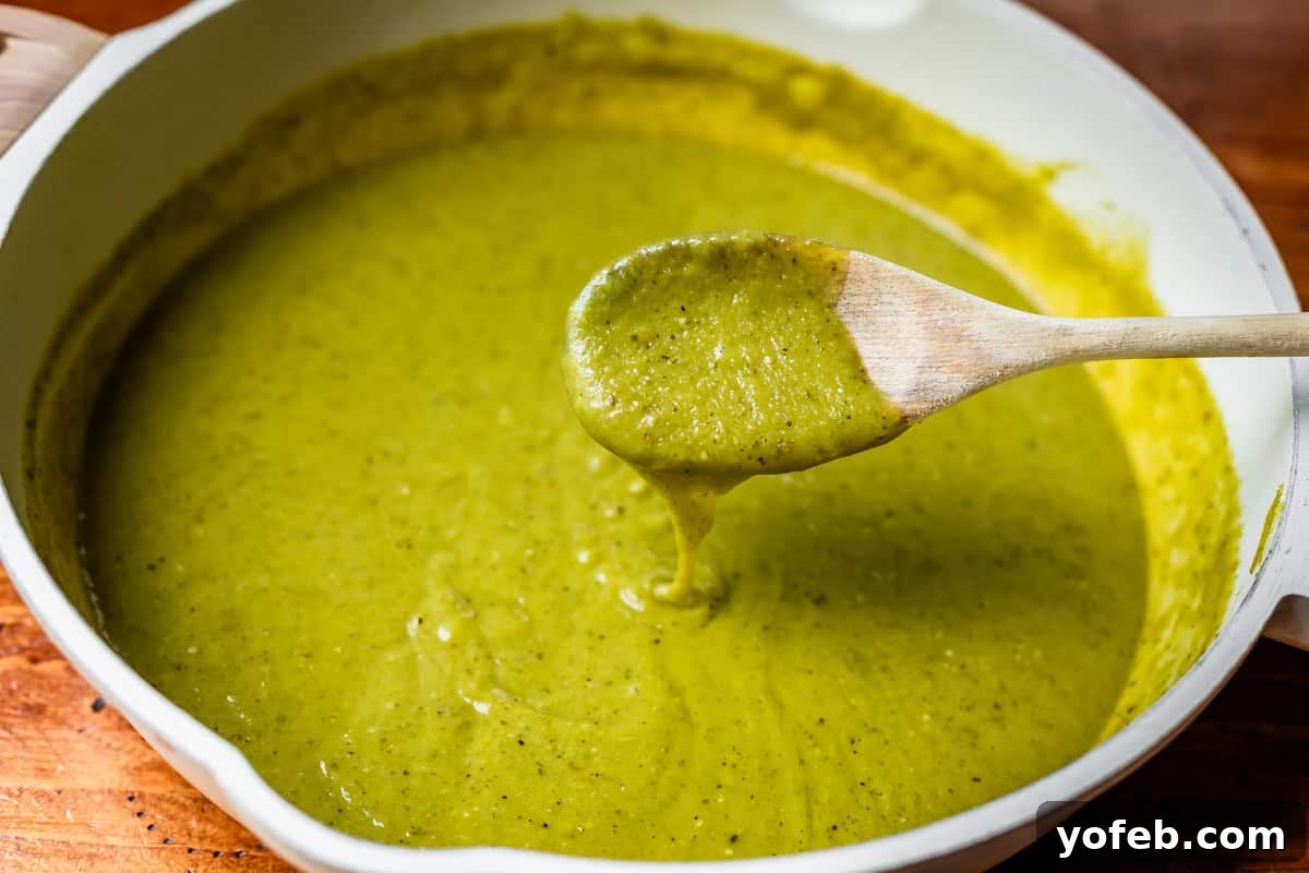 Yeni Gözdem Tavuk Enchilada 9 wooden spoon dipping into blended green enchilada sauce in a frying pan.