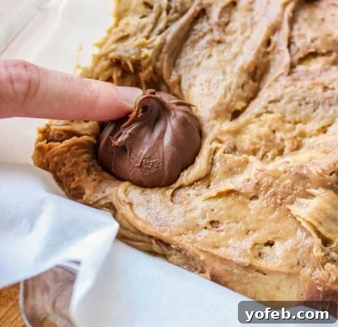 Blondie batter spread in a baking pan with frozen Nutella dollops pressed into it, ready for baking.
