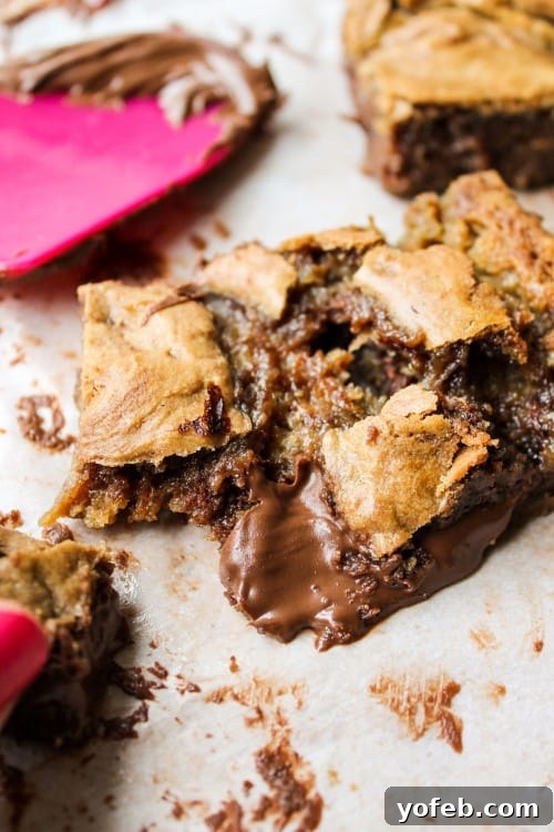 A Nutella-stuffed blondie, still warm and gooey, cut and lifted from the pan, illustrating the challenge of eating them hot.