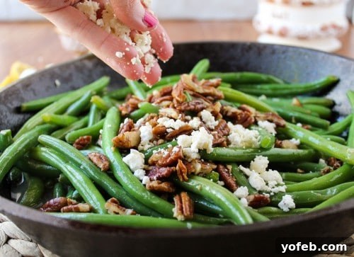 Adding chopped fried pecans and crumbled feta cheese to the cooked green beans.