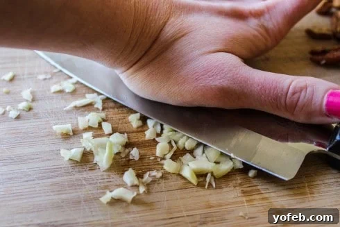 A chef's knife crushing garlic cloves on a cutting board, preparing for the lemon-garlic mixture.