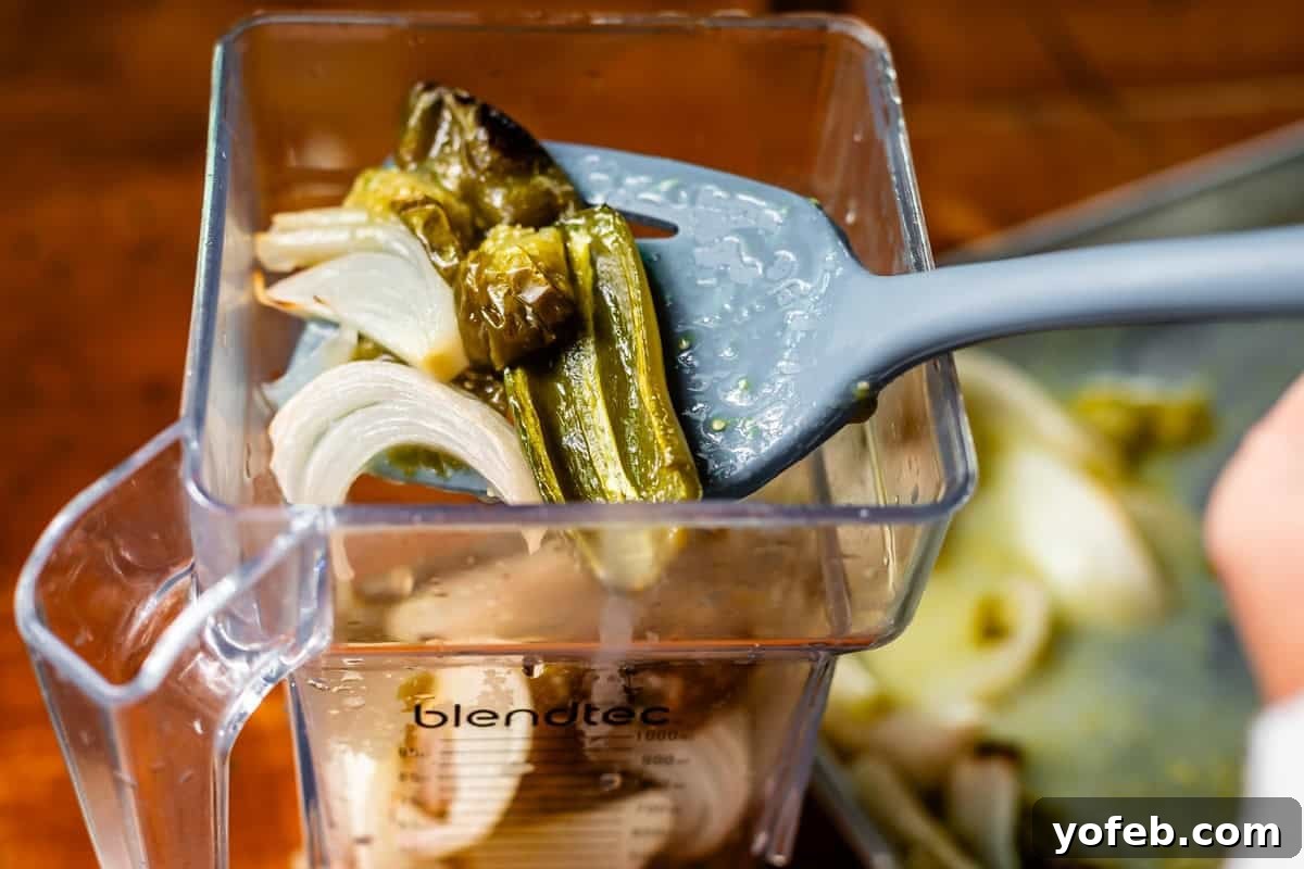 Tangy Tomatillo Enchilada Sauce 11 spatula holding roasted onion and jalapenos adding them to a blender.
