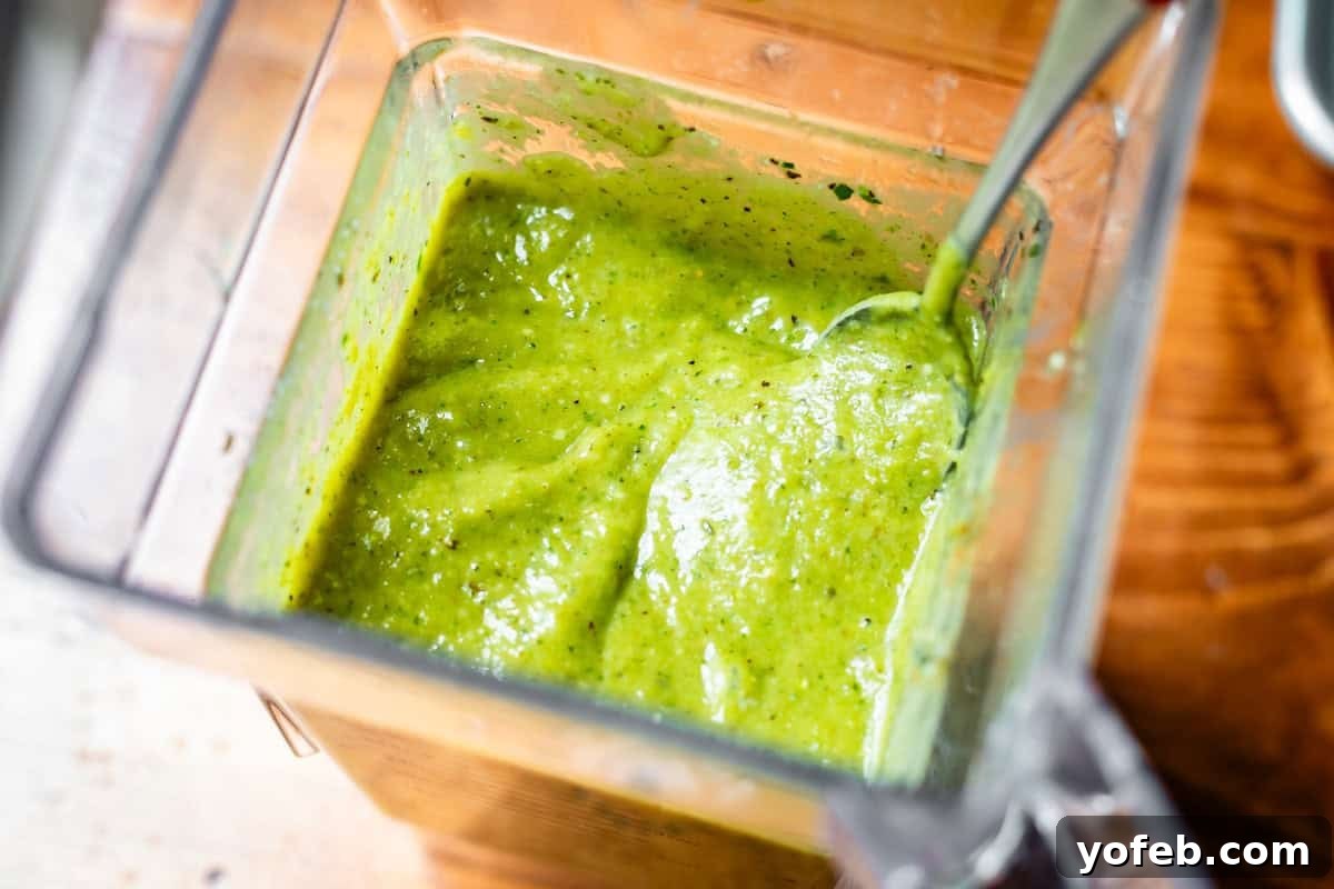 Tangy Tomatillo Enchilada Sauce 15 a blender with a metal spoon inside scooping up some green enchilada sauce.