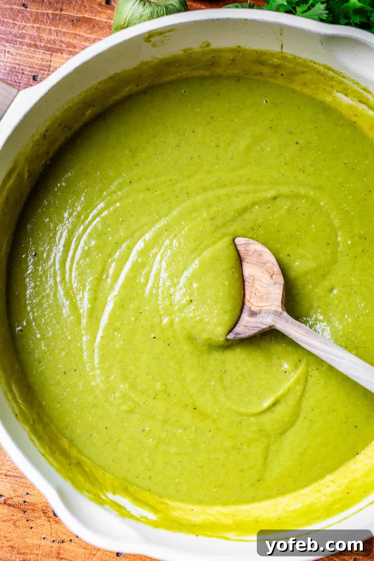 Tangy Tomatillo Enchilada Sauce 18 a large skillet filled with green enchilada sauce with a wooden spoon stirring it.