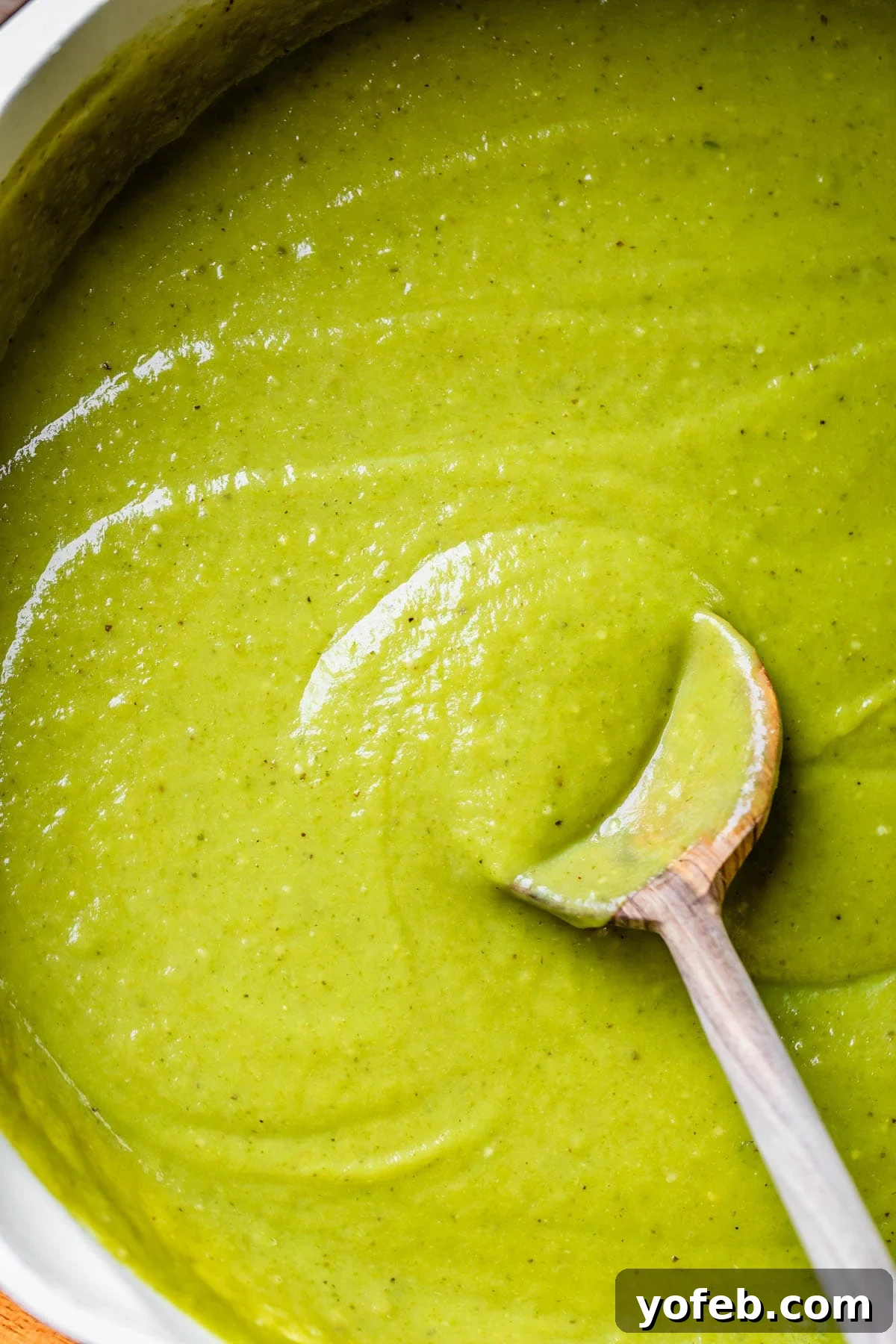 Tangy Tomatillo Enchilada Sauce 5 a large skillet filled with green enchilada sauce with a wooden spoon stirring it.