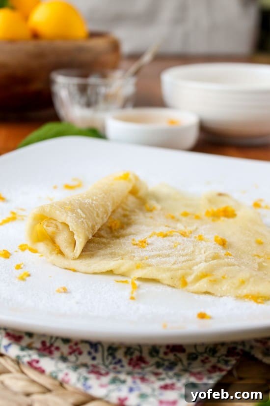 Zesty Meyer Lemon & Cardamom Crepes 8 lemon crepe in the process of being rolled up from a fold with sugar sprinkled on top along with lemon zest
