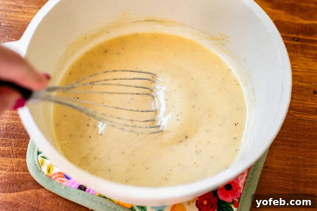 Laura's Sumptuous Tomato Bisque 12 A flat whisk stirring a finished, creamy white sauce, demonstrating its smooth, lump-free consistency.