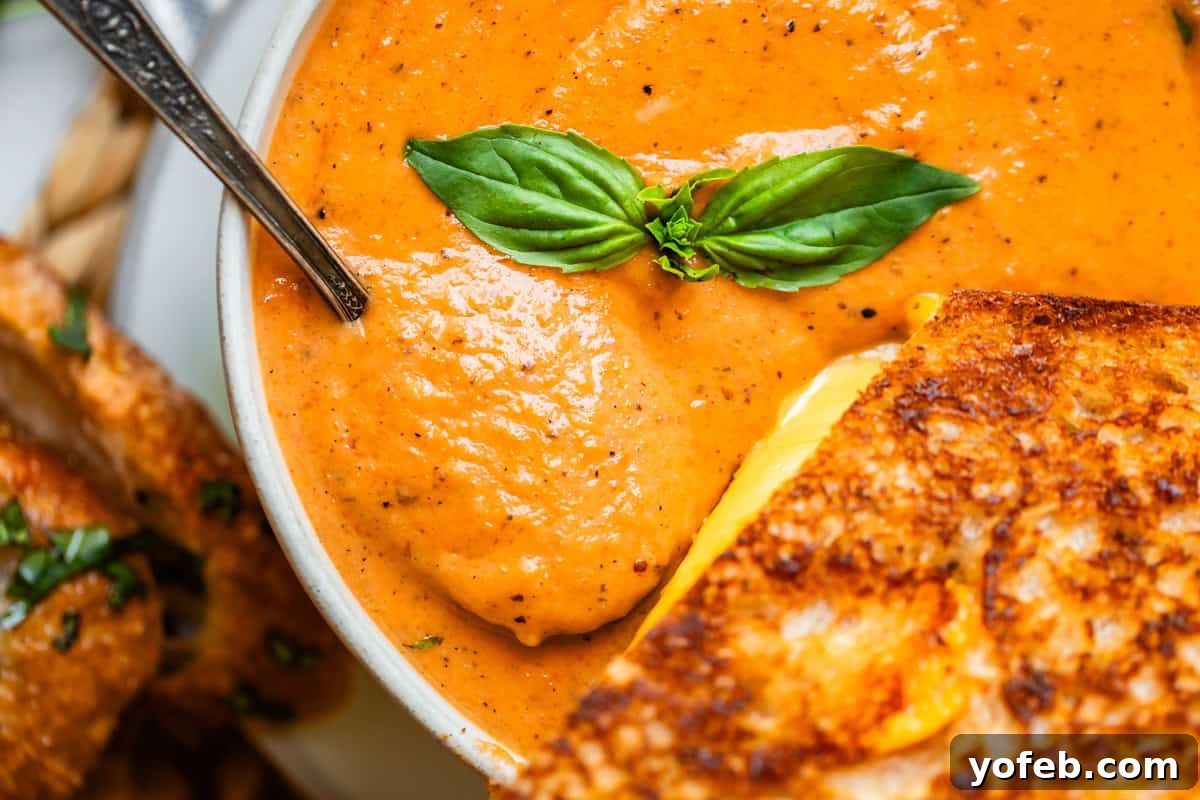 Laura's Sumptuous Tomato Bisque 15 A close-up view of a bowl of creamy tomato bisque with a metal spoon and a slice of grilled cheese, ready to be enjoyed.