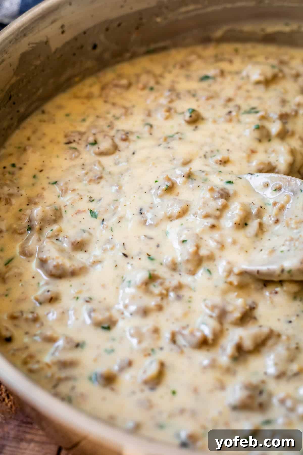 Fluffy Biscuits, Savory Gravy 17 creamy sausage gravy being stirred by a wooden spoon in a metal pan.