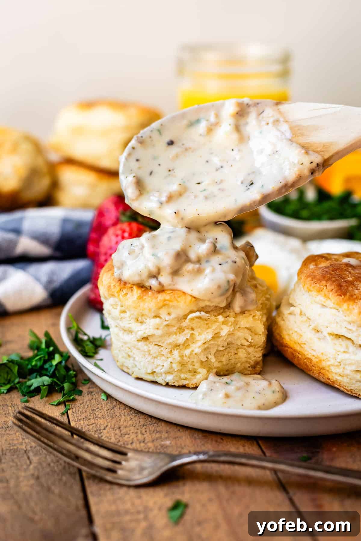 Fluffy Biscuits, Savory Gravy 19 wooden spoon pouring sausage gravy over the top of biscuits on a ceramic plate.