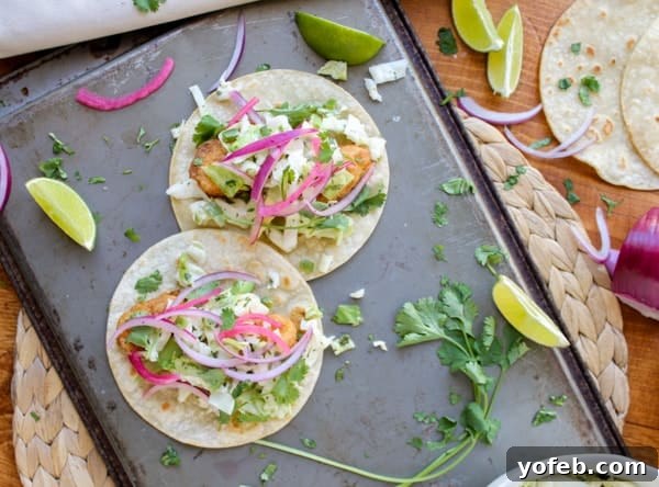 Freshly Assembled Baja Fish Tacos Two vibrant fish tacos garnished with fresh cilantro, lime wedges, red onion, and slaw, arranged on a baking sheet.