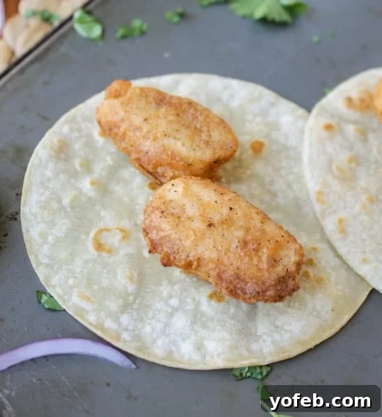 Crispy Beer Battered Fish Fillets for Tacos Two pieces of golden-brown battered fish laid on a warm corn tortilla, ready for toppings.