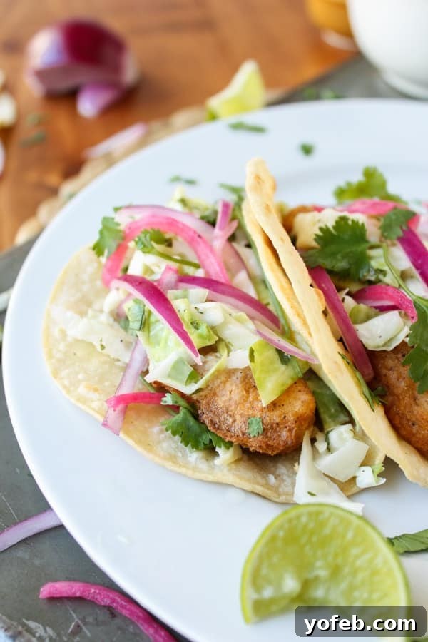 Gourmet Baja Fish Tacos Plated Two beautifully presented battered fish tacos on a white plate, garnished with fresh slaw, red onions, and a lime wedge.